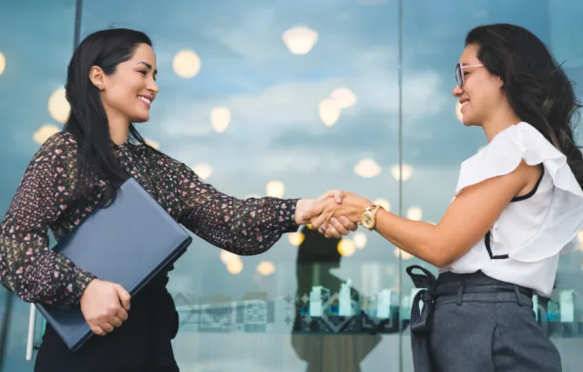 Foto de dos mujeres saludandose de mano una en frente a otra
