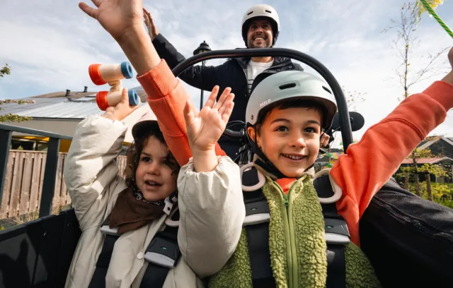 Foto de dos niños disfrutando en una montaña rusa, están alzando las manos