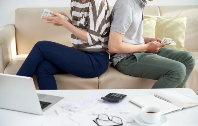 Foto de dos personas de espaldas contanto dinero sobre un sofa