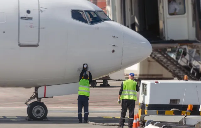 Foto de la trompa de un avión con dos personas debajo 