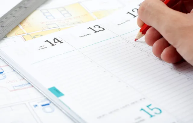 Foto de un calendario genérico con una mano encima y una persona escribiendo sobre él
