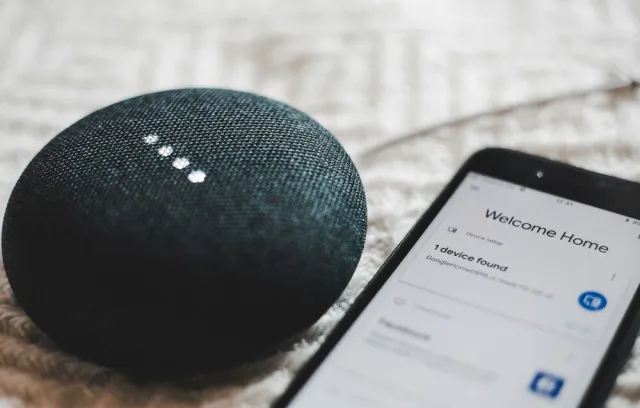 Foto de un celular y una alexa al costado, dispositivo electrónico