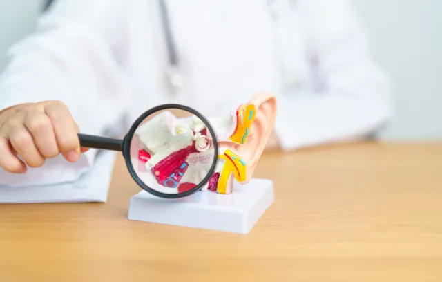 Foto de un doctor mostrando una lupa sobre un oído humano
