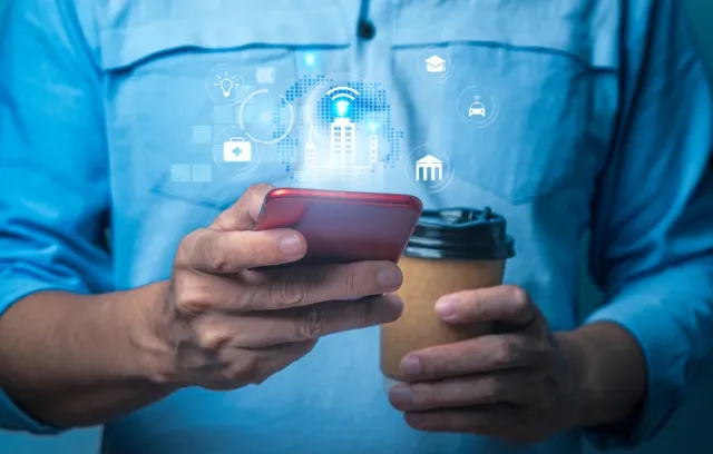 Foto de un hombre utilizando su celular en una mano y con un café en la otra