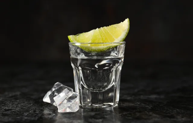 Foto de una copa para tomar licor con un limón encima y un fondo negro