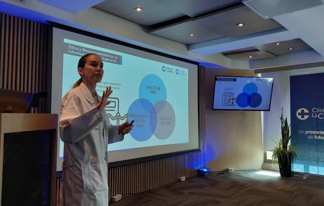 Foto de una doctora hablando frente a una pantalla 