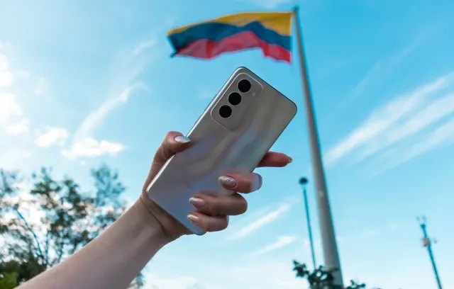 Foto de una mano de mujer con un celular y una bandera de fondo