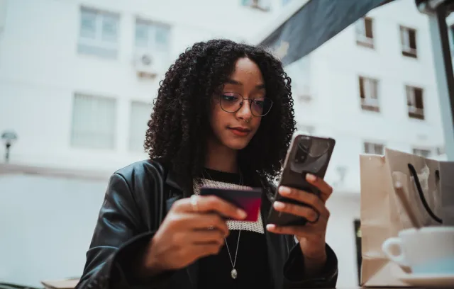 Foto de una mujer con un celular en la mano y una billetera en la otra