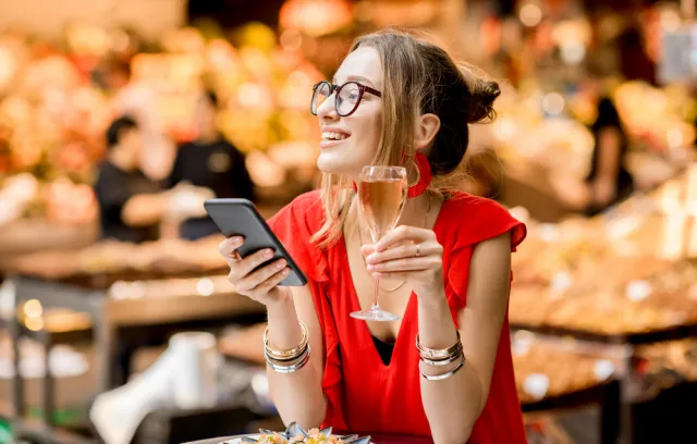 Foto de una mujer con un celular en la mano y una copa en la otra