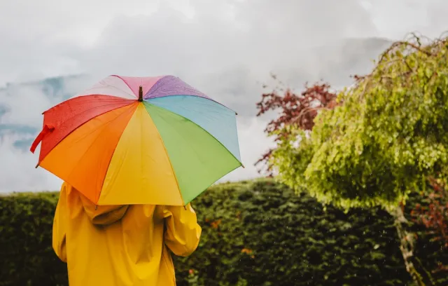 Foto de una mujer con un paraguas abierto de varios colores  de fondo a la cámara