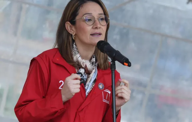 Foto de una mujer hablandole a un microfono con una chaqueta roja