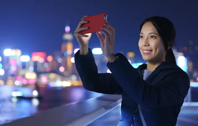 Foto de una mujer tomando una fotografía al cielo con un fondo de una ciudad alumbrada
