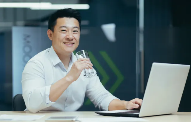 Foto de una persona asiática tomando agua con un computador en su mano