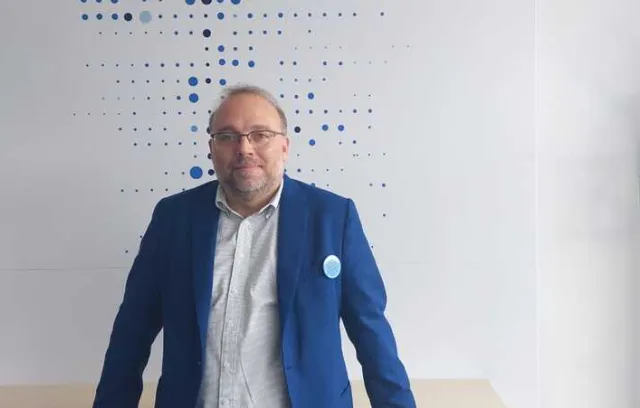 Foto de una persona con brazel y camisa azul mirando a la cámara