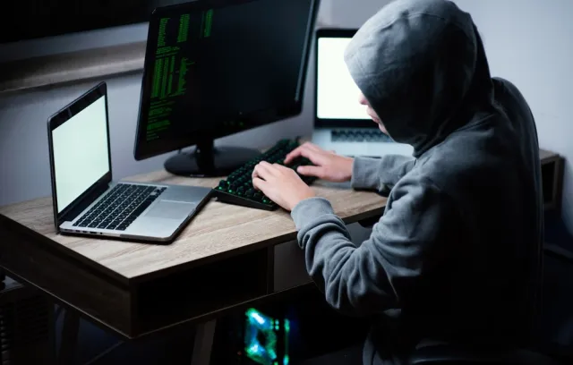 Foto de una persona con una capucha trabajando con un computador 