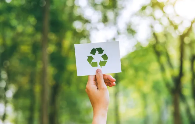 Foto de una persona mostrando con una mano el símbolo de reciclaje con un fondo verde