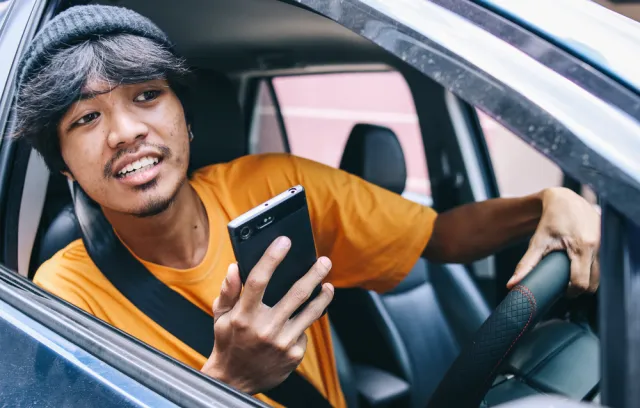 Foto de una persona sacando la cabeza por la ventana con un celular en la mano