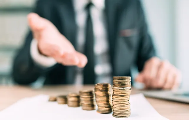 Foto de unas monedas apiladas y de fondo un señor de traje