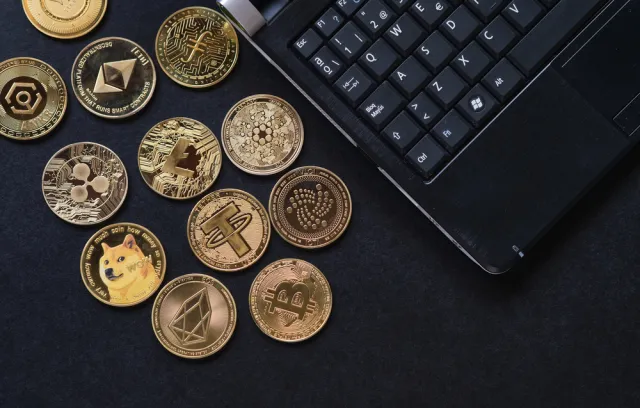 Foto de varias monedas cripto sobre una mesa con un computador al costado derecho