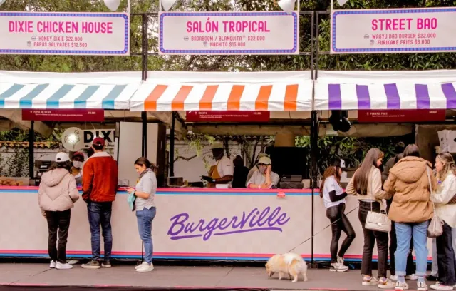 Foto de varias personas haciendo fila frente a unos locales de colores pastel