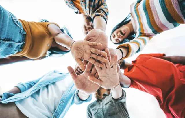 Foto de varios jovenes juntando sus manos en la mitad