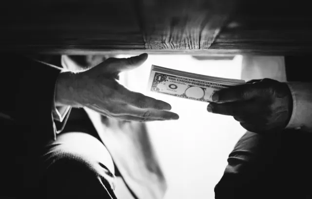 Foto de dos personas pasando dinero por debajo de la mesa