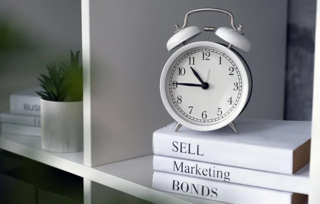 Fotografía de tres libros blancos y un reloj encima