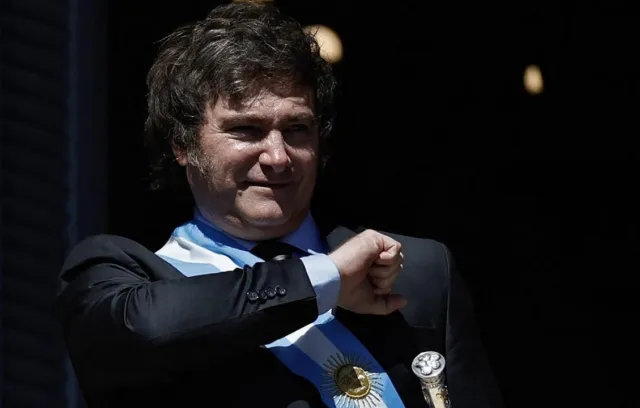 Fotografia de una persona con pelo en la frente y traje con una bandera de argentina en su costado