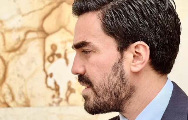 Foto de perfil de Gabriel Santos, un hombre barbudo con corbata posando de medio lado hacía la cámara