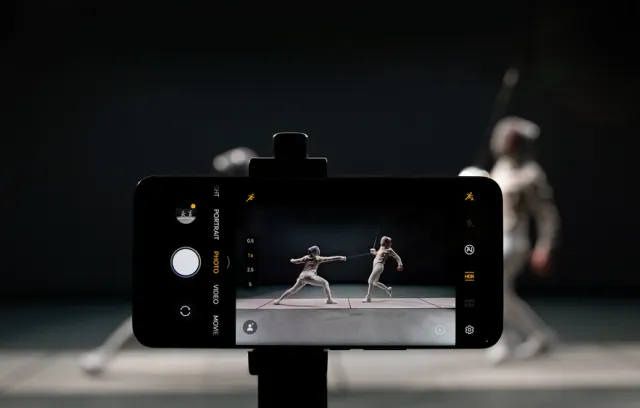 Foto de una celular tomando una foto de dos personas jugando esgrima con fondo negro