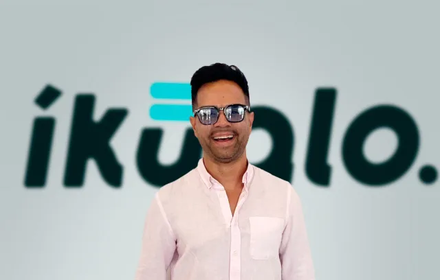 Fotografía de un hombre sonriendo con unas gafas y de fondo el nombre de Ikualo