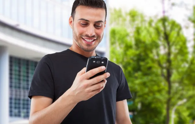 Foto de un hombre mirando al celular mientras sonrie