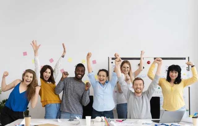 Foto de personas alzando las manos y sonriendo en sus oficinas