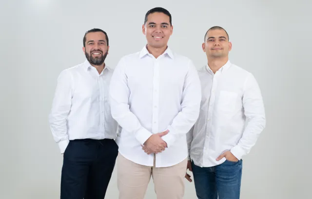 Fotografía de tres hombres con camiseta blanca mirando a la cámara