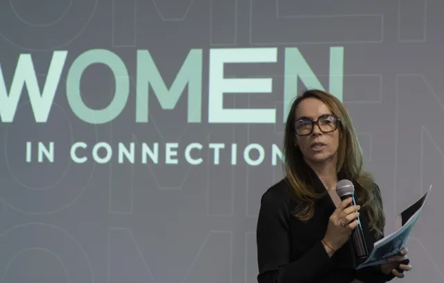 Mujer hablando en un escenario profesional con un fondo que dice Women