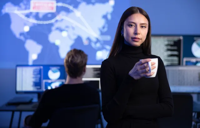 Mujer mirando a la cámara con un fondo de una persona trabajando en un computador y un diseño de continentes arriba de él