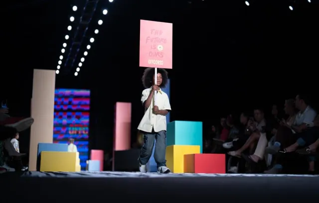 Niño caminando por una pasarela con un cartel encima