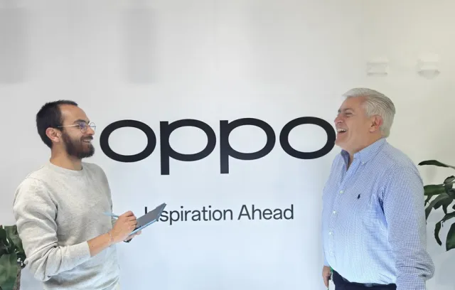 Fotografía de dos personas hablando con un letrero de fondo que dice Oppo