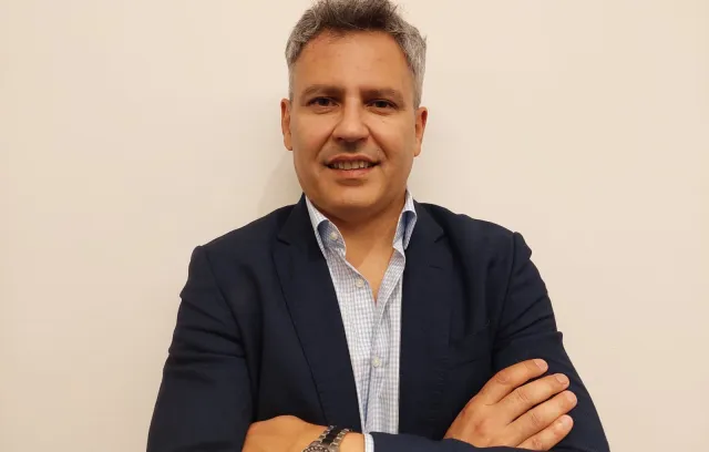 Foto de una persona posando frente a la cámara, cuenta con camiseta, blazer negro, reloj y pelo blanco