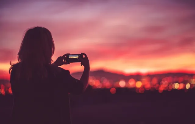 Una mujer tomando una foto sobre un cielo rosado y naranja