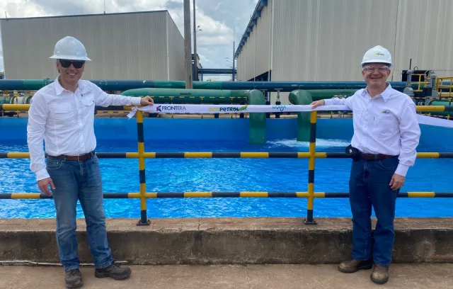 foto de dos personas frente a una planta de tratamiento de agua con camiseta blanca