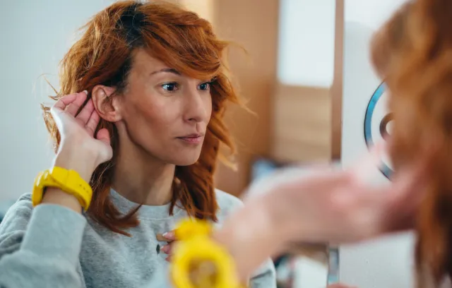Una mujer tocandose la oreja frente al espejo