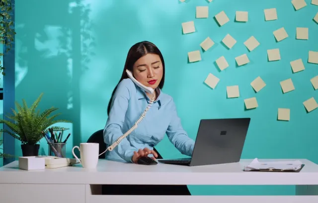 Mujer hablando por teléfono, mirando el computador y con muchos stickers pegados en la pared