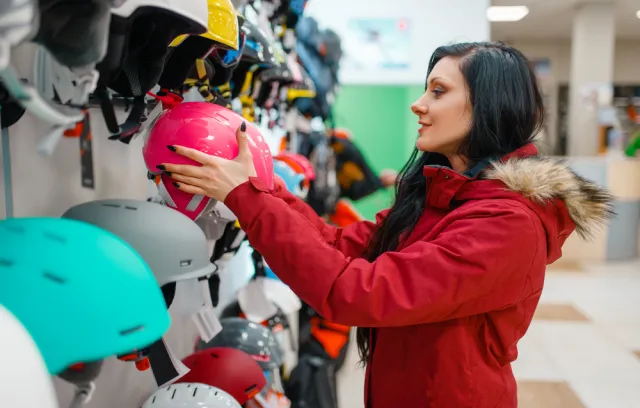 Una mujer con chaqueta roja toma un casco  rosado de un local 