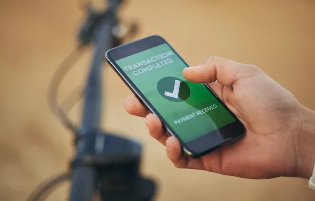 Foto de una mano sosteniendo un celular con una pantalla verde que dice transacción exitosa