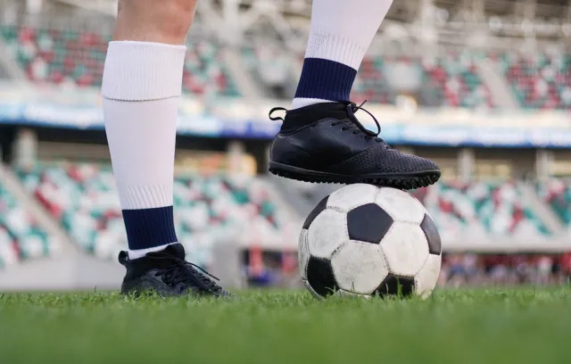 Foto de una persosona con guaybos y un balón de fútbol sobre su pie derecho