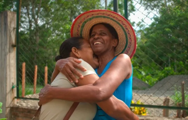 Mujeres abrazandose, una de ellas tiene un sombrero colorido