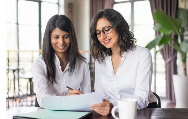 dos mujeres sentadas mirando una hoja de papel que tienen al frente