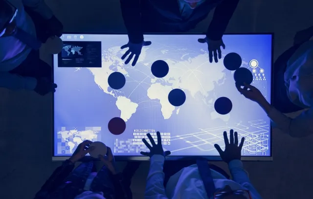 personas reunidas sobre un tableto azul, solo se ve la silueta de las manos