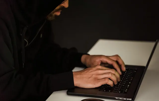 un hombre con capucha negra escribiendo en su laptop